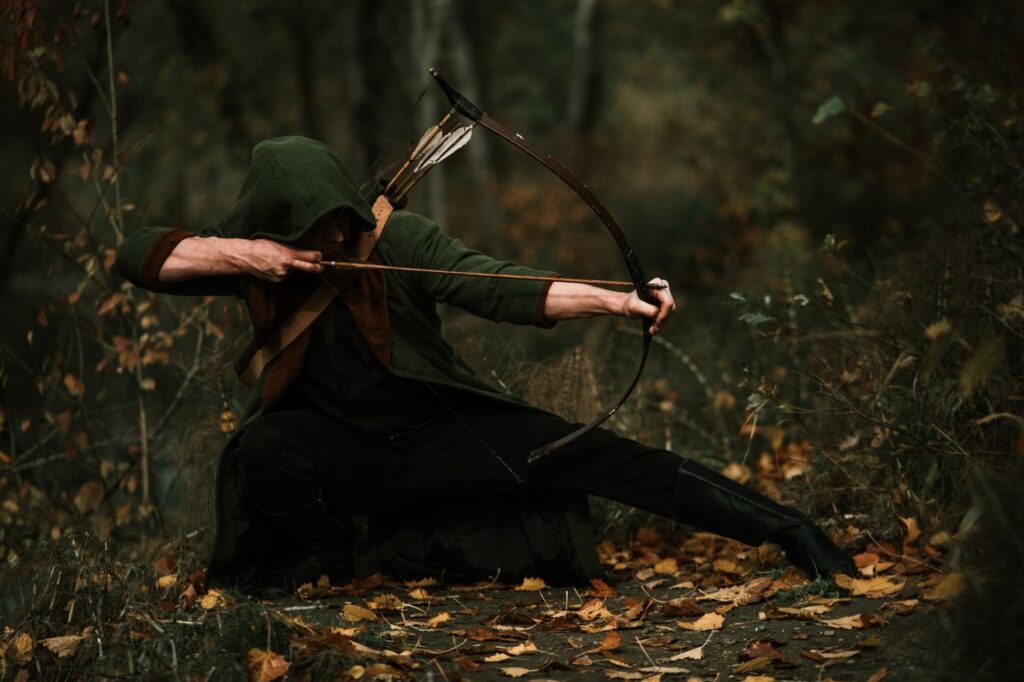 Medieval archer crouched in forest, aiming a bow with precision. Autumn foliage surrounds.